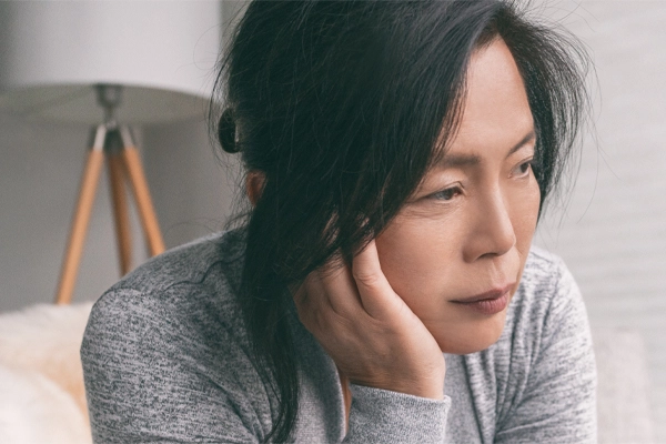 A middle-aged asian woman sitting on her couch, resting her head on her hand, suffering from adrenal fatigue. Get treatment for adrenal fatigue syndrome from Blue Skye Health and Wellness in Tampa.