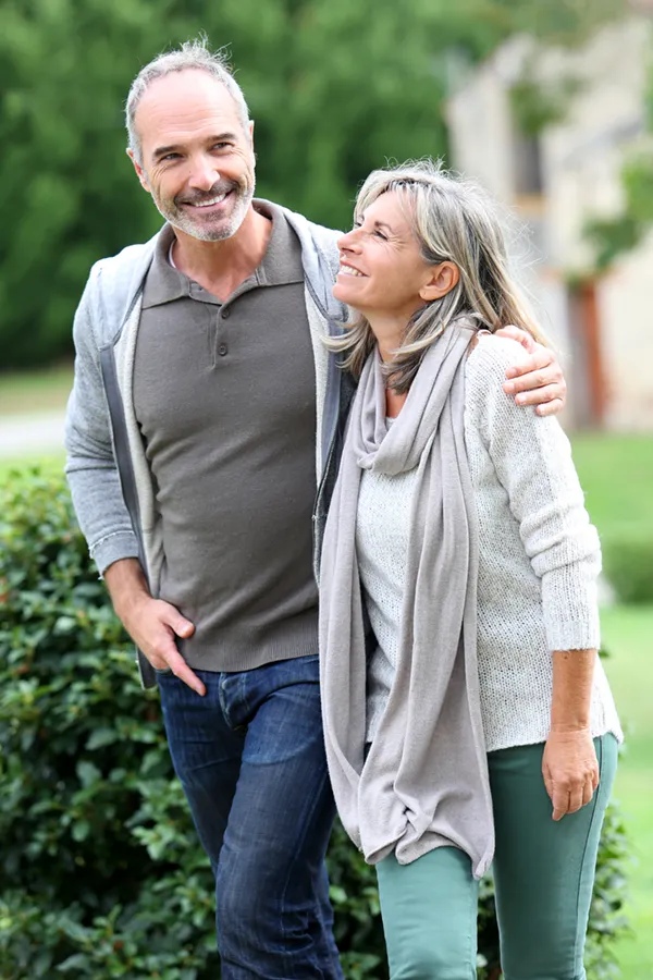 A mature couple in gray toned clothes and jeans walk happily outside, happy with their successful bioidentical hormone treatments from Blue Skye Health and Wellness in Tampa.