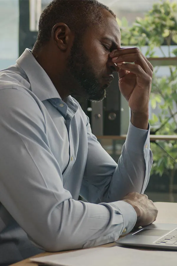 A black man rubbing the top of his nose at his desk, in need of chronic fatigue treatment from Blue Skye Health and Wellness in Tampa.