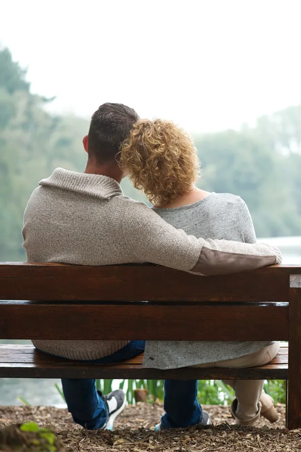 A man with his arm around a woman are shown from behind sitting on a bench on a serene morning. Get integrative medicine treatment from Blue Skye Health and Wellness in Tampa.
