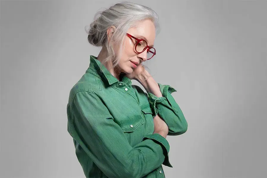 A middle-aged woman in a green shirt holds her neck and grimaces in pain. Schedule low dose naltrexone treatment from Blue Skye Health and Wellness in Tampa.