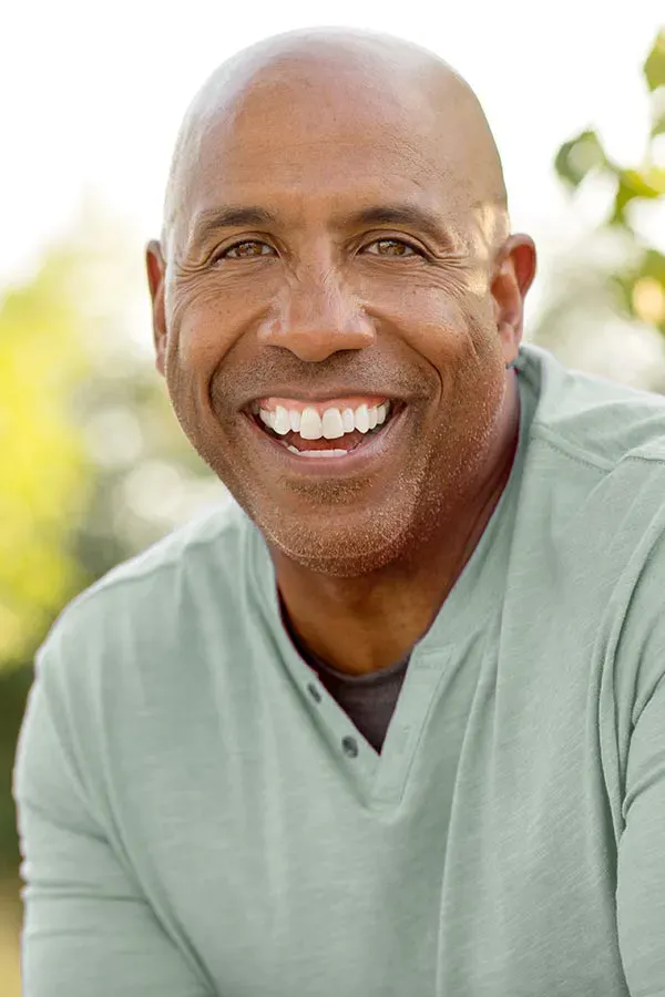 A man in a green shirt sits outside smiling and pain-free. Get low dose naltrexone treatment from Blue Skye Health and Wellness in Tampa.