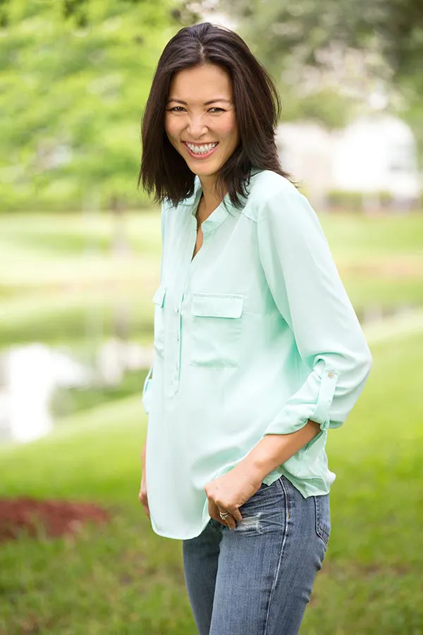 A middle-aged brunette woman in a light green button-up shirt stands outside smiling, happy with her perimenopause treatment from Blue Skye Health and Wellness in Tampa.