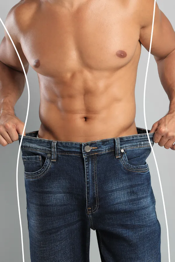 A strong shirtless man in jeans holds the waistlines of his too-big jeans to show the success of semaglutide weight loss from Blue Skye Health and Wellness in Tampa.