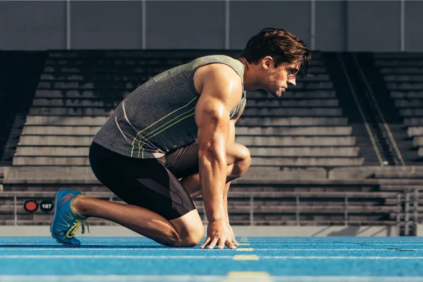 With a determined look, A muscular man in track clothes kneels at the start of a race. Get Sermorelin peptide therapy from Blue Skye Health and Wellness in Tampa.