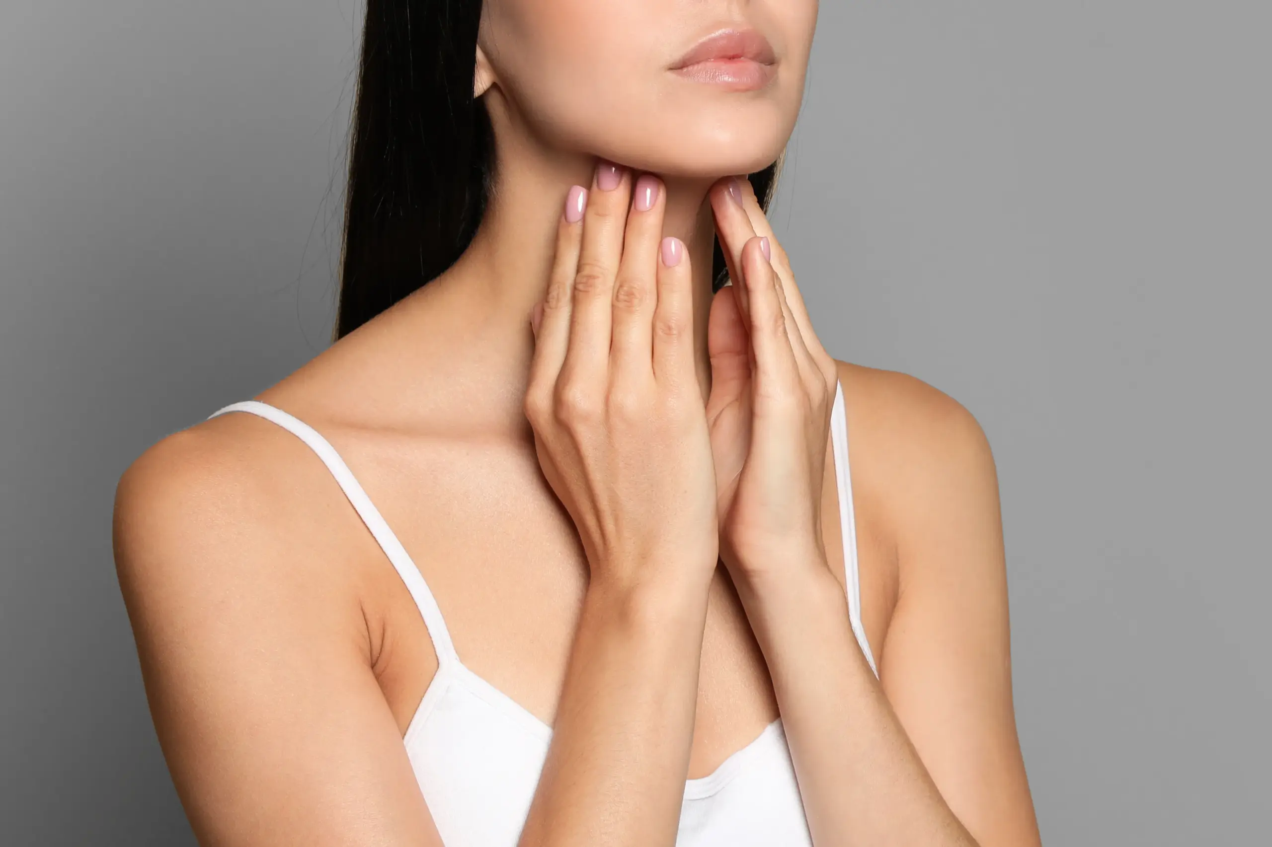 A woman in a white tank top touches her neck looking for signs of thyroid disorder. Get help for thyroid disorders from Blue Skye Health and Wellness in Tampa.