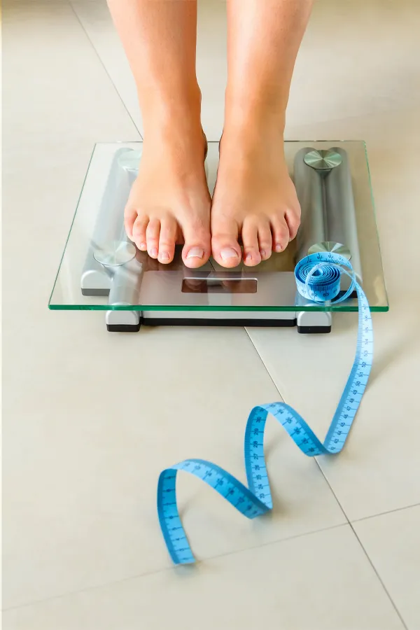 Close-up of a woman's feet standing on a scale, with measuring tape by her toes, getting treatment for weight loss resistance from Blue Skye Health and Wellness in Tampa.